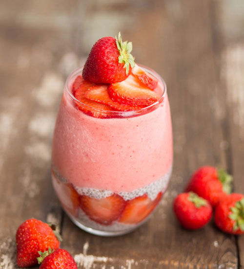 Strawberry smoothie in a glass with fresh strawberries, blurred wooden background