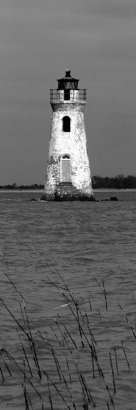 A lighthouse in the water in black and white.