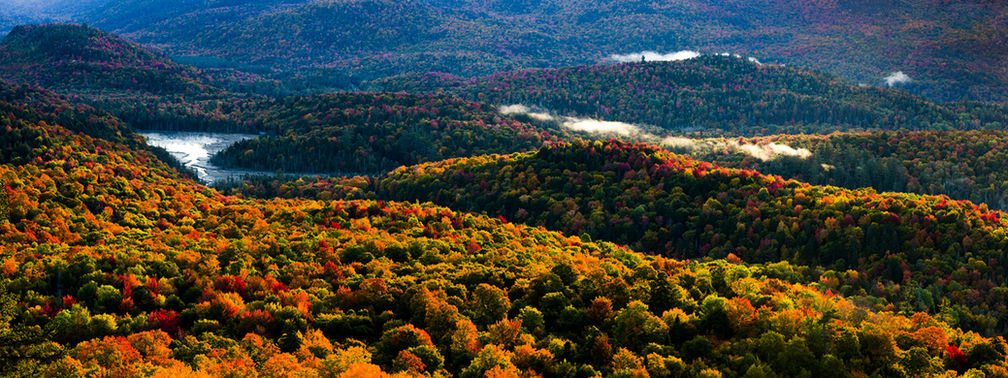 A valley covered in fall foliage with a lake and some small clouds.