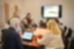 VBG commercial pre-construction services : our team collaborates over architectural plans at a wooden table. A screen displays data above them, creating a focused atmosphere.