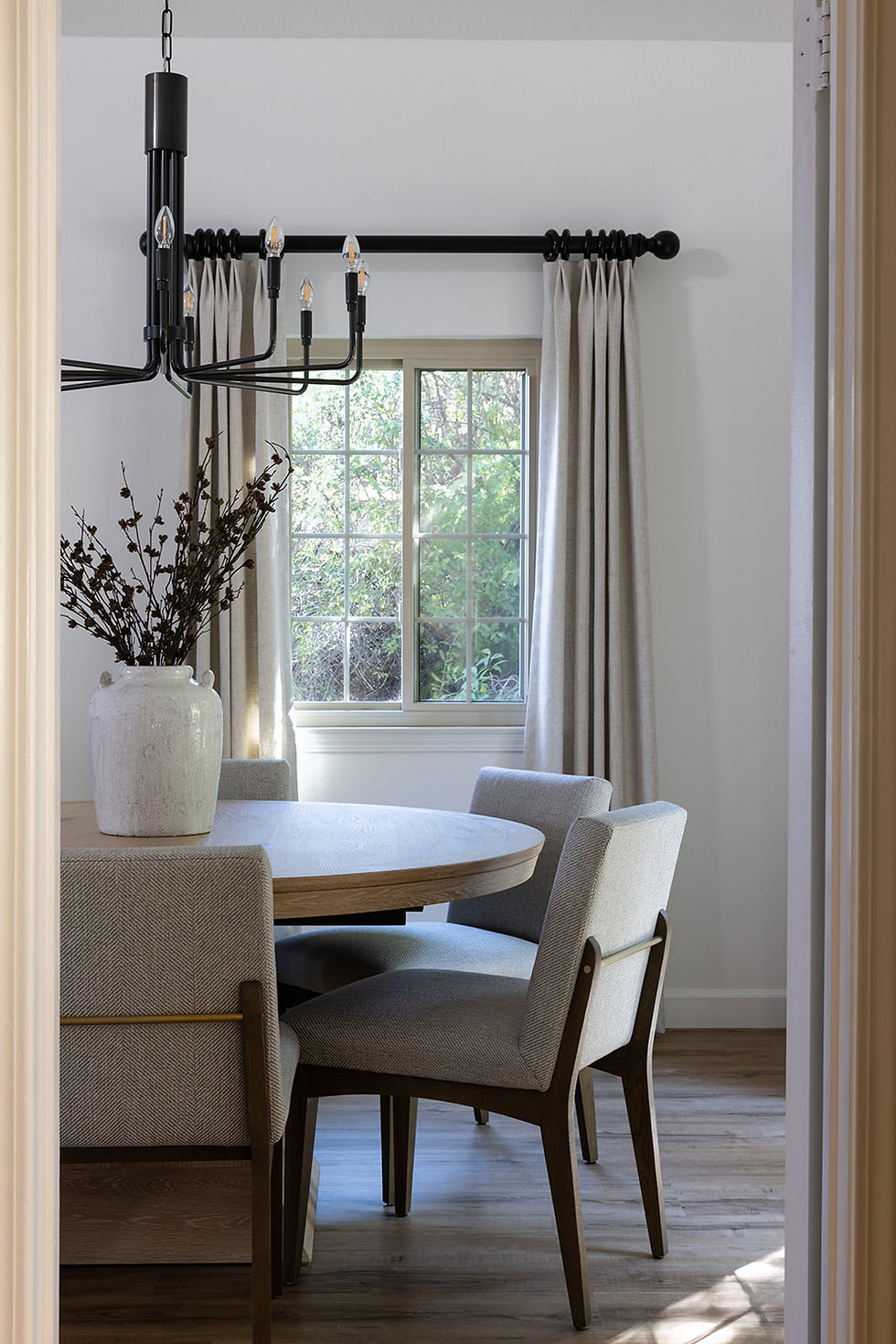 Contemporary dining room with round wood table, upholstered dining chairs, black chandelier and custom window treatments by Ethan Charles Design
