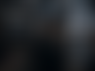 An emotionally exhausted individual standing still in a fast-moving modern city surrounded by blurred lights, crowds, and overwhelming stimulation.