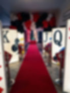 Themed event entrance with a red carpet flanked by giant playing card cutouts, oversized dice, and a balloon arch.