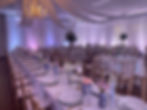 Indoor ballroom reception featuring long banquet tables, blue and white Chinoiserie vases, gold chairs, and overhead fabric swags with a crystal chandelier.