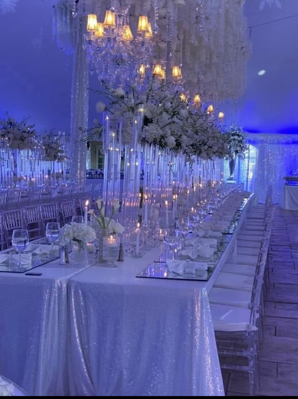 Elegant dining set up with white table cloth, crystal clear chairs with flowers as a centerpiece.