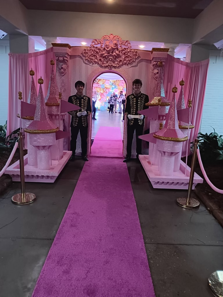Entrance to a themed party with two greeters dressed up in uniform with a pink carpet leading to the door.