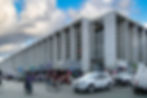 Exterior view of Mercado San Benito in Mérida, showing the large concrete building with busy street activity, market stalls, cars, and people gathered at the entrance.