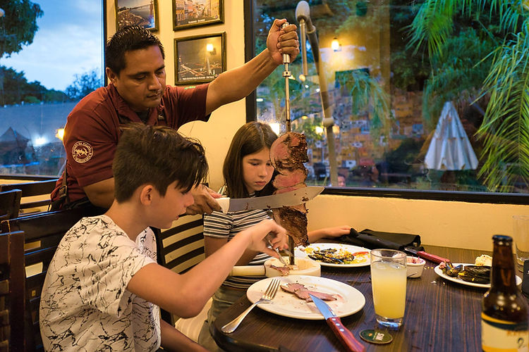 Server slicing grilled meat tableside for children at Churrascaria Rancho Da Picanha in Mérida, a popular Brazilian all-you-can-eat steakhouse with a cozy family-friendly atmosphere.