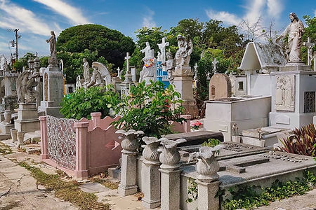 Gravestones and statues at Cementerio General in Mérida, featuring ornate tombs, lush greenery, and historic monuments under a clear blue sky.