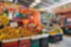 Fruit stall inside Mérida’s San Benito Market with crates stacked high with mangoes, papayas, dragon fruit, melons, grapes, and bananas, displayed under hanging lights and festive decorations.