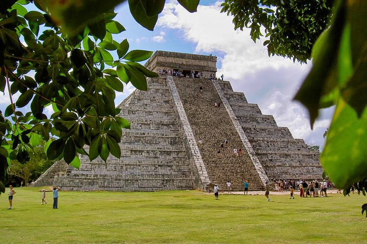 View of the Kukulkan Pyramid at Chichén Itzá, Yucatán, Mexico – iconic Mayan temple framed by trees, known for its equinox serpent shadow and UNESCO status.