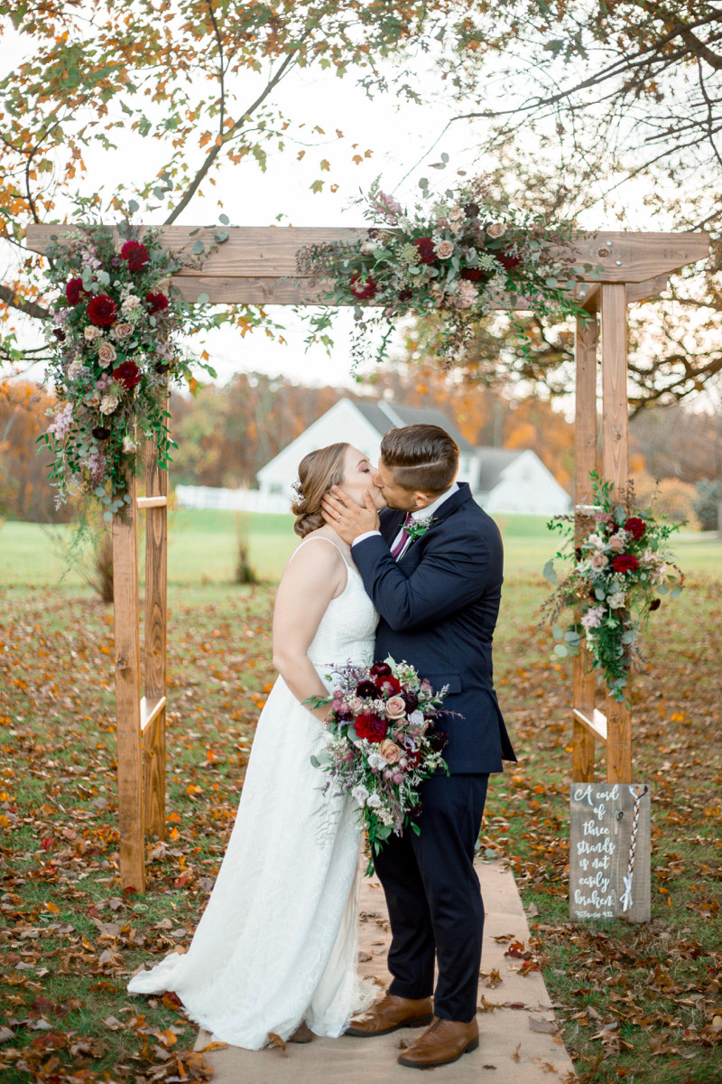 Married couple kissing under wedding arch. Photo by Laura Gares photography.