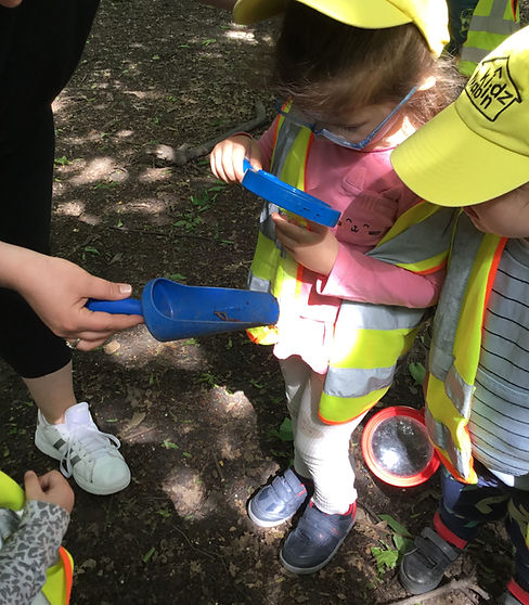 Two children with magnifying glasses from Kidz Kabin Nursery in Muswell Hill on an outdoor adventure trail and learning about the earthworm their teacher collected in her spade.JPG