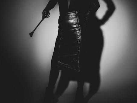 Ulla Burns draped in a leather skirt holding crop-Mistress NYC