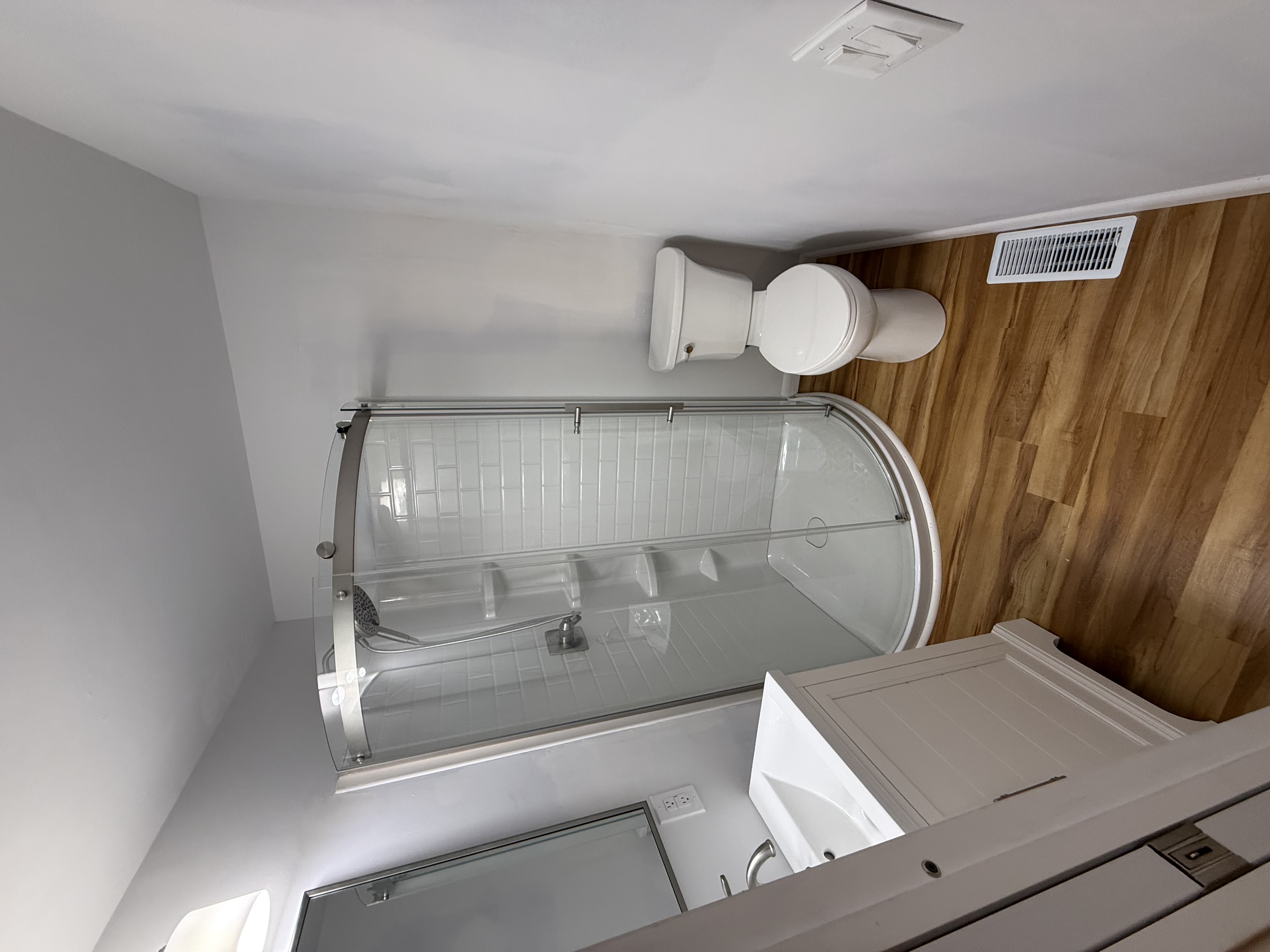JM bathroom with a glass corner shower and wood-look flooring