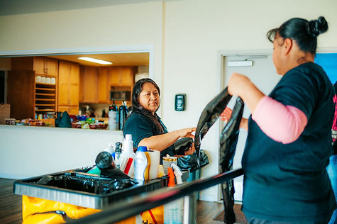 two woman by a cleaning cart getting trash bags and cleaning supplies