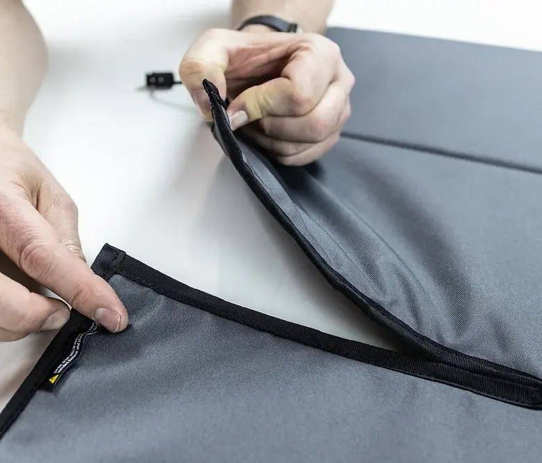 Hands demonstrating Van Essential demo: closing gray fabric with black zipper and trim.