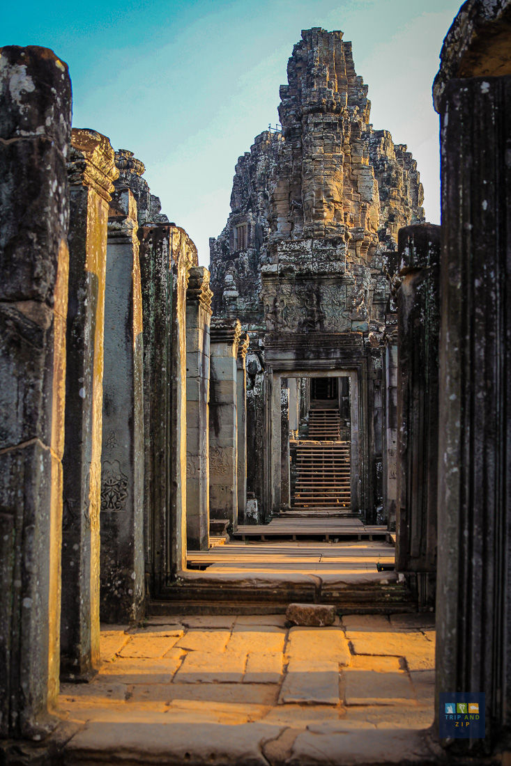 Ancient stone temple corridor with carved details, lit by warm sunlight. Eroded archways lead to a central tower. Peaceful ambiance.
