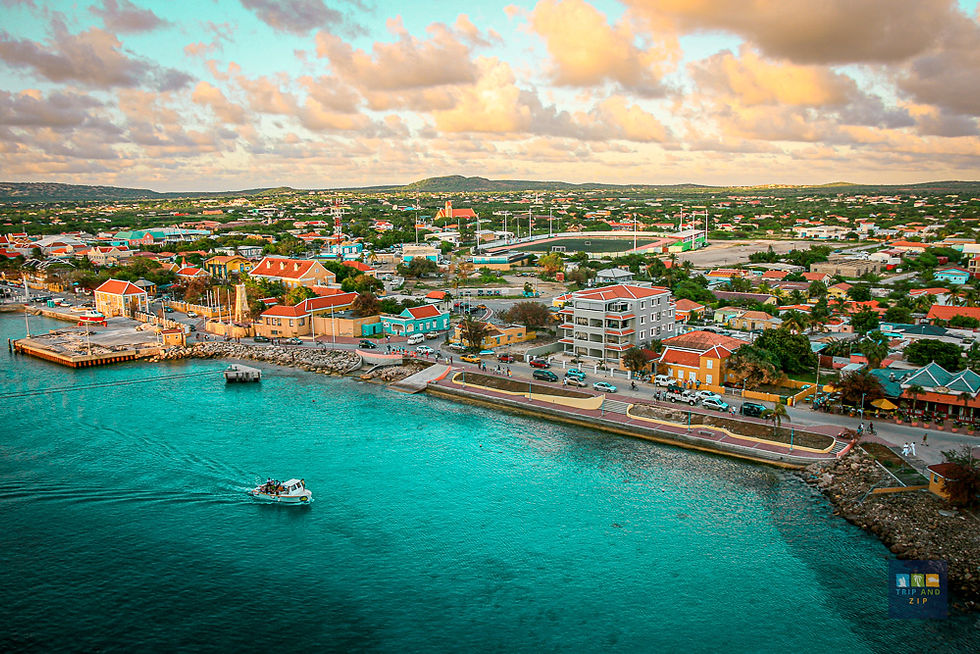 Aerial view of a colorful seaside town with a boat on turquoise water, vibrant houses, and a bright sky with clouds; a peaceful scene.