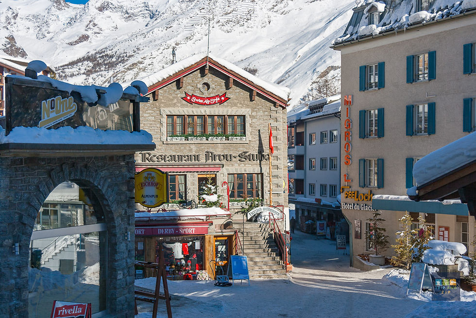 Snowy Swiss village street with a stone restaurant and colorful signs. Sunny day, snow-covered mountains in the background, festive mood.