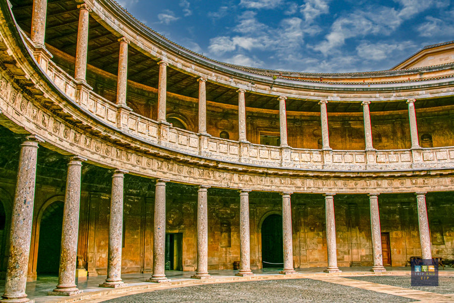 Circular courtyard of a historical building with stone columns, intricate arches, and a cobblestone floor under a blue sky.
