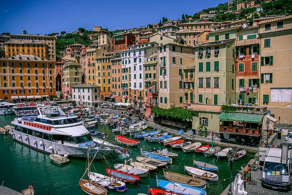 Colorful boats and a large yacht docked in a charming Italian harbor, surrounded by vibrant buildings under a clear blue sky.