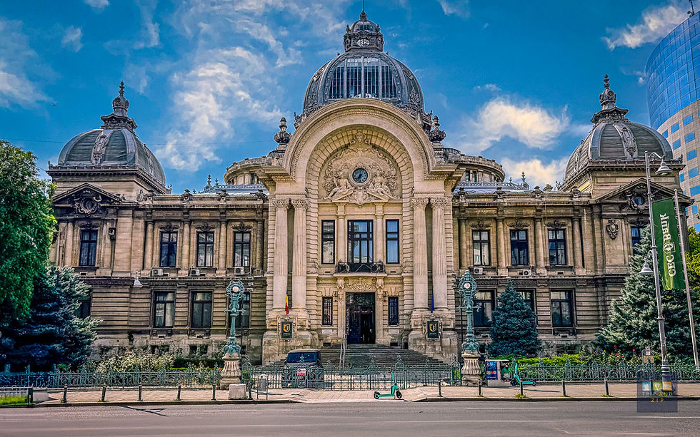 Ornate historical building with detailed domes and columns against a partly cloudy sky. Romanian flag visible, modern building in background.