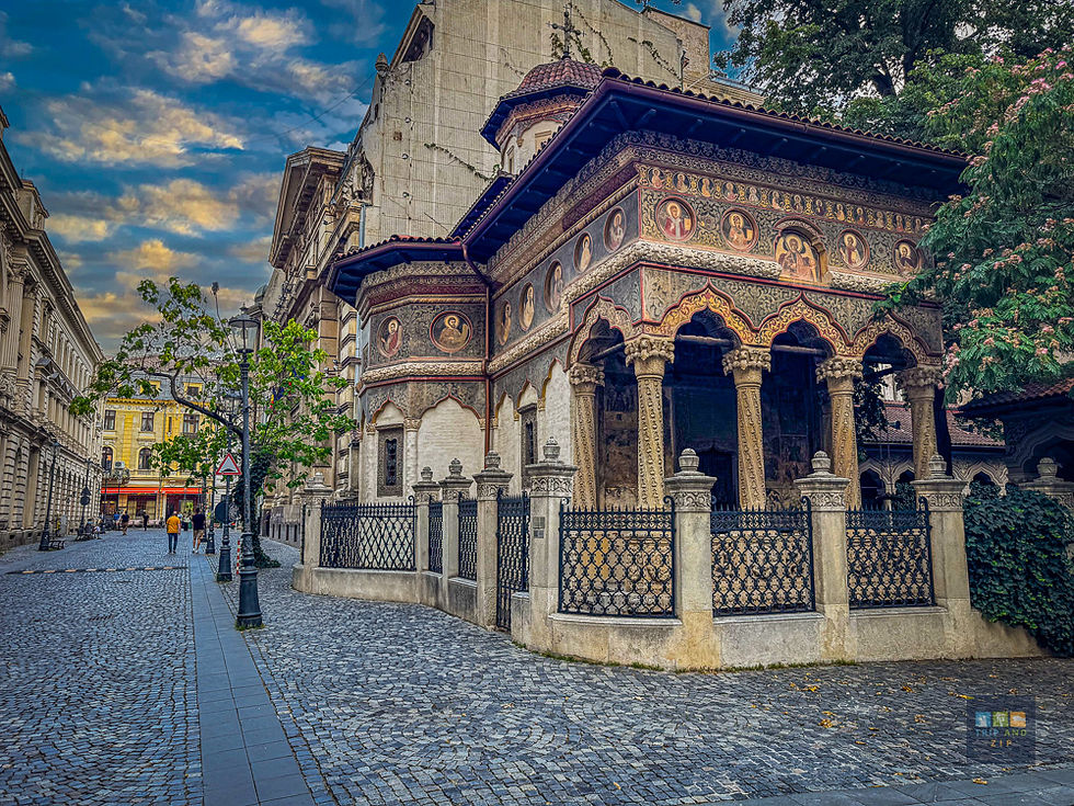 Historic building with ornate arches and frescoes on a cobblestone street. Trees and a lamppost nearby under a partly cloudy sky.