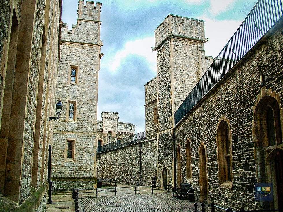 Stone tower buildings with arched windows and a cobbled walkway under a cloudy sky. Black railings line the path, creating a historic mood.