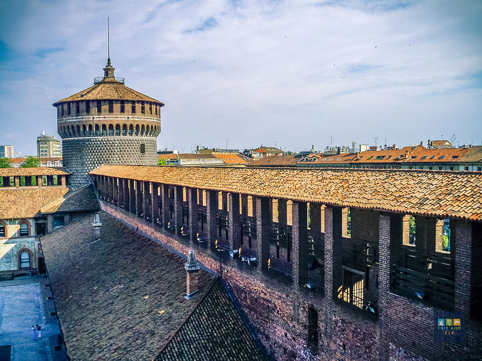 View of a historic brick castle with a tower and arched roof. Sunny day, blue sky. City buildings visible in the background.