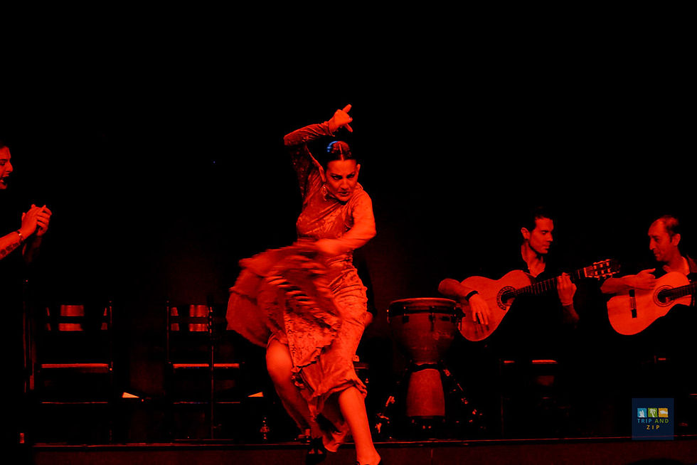 Flamenco dancer in red dress energetically performs on stage, flanked by two guitarists. Dark background enhances the dramatic mood.