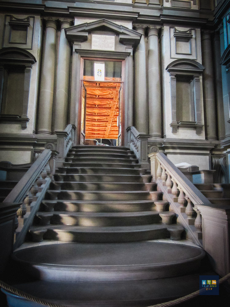 Grand staircase leading to an ornate wooden door, framed by classical columns. Warm light from inside, modern building exterior.