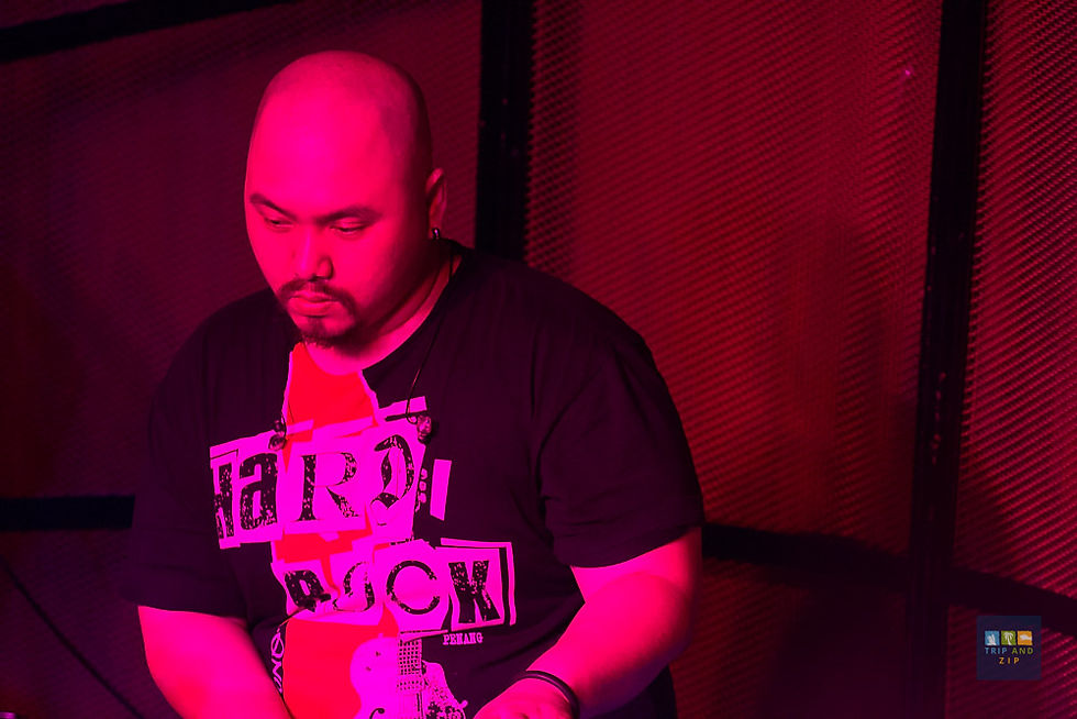 A person with a bald head is wearing a "Hard Rock" t-shirt, focused in a dimly lit pink room. "TRIP AND ZIP" text is visible below.