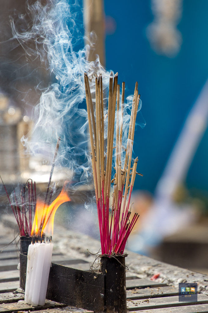 Burning incense sticks with smoke and a lit white candle against a blurred blue background, creating a peaceful, spiritual atmosphere.