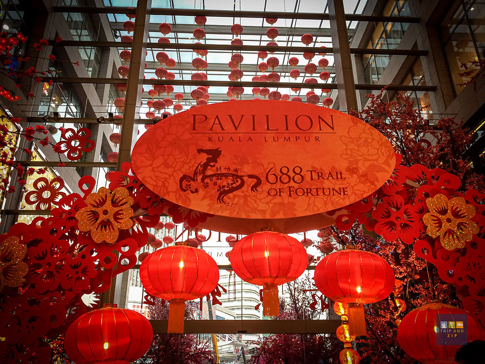 Red lanterns and floral decorations hang in Pavilion Kuala Lumpur. A sign reads "688 Trail of Fortune," creating a festive, vibrant mood.