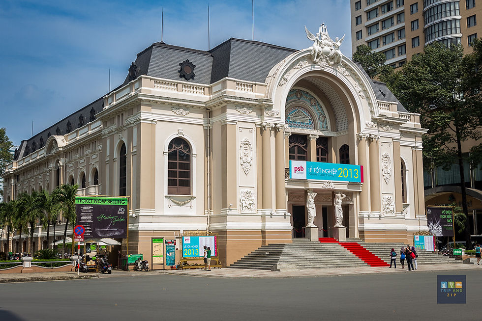 Historic building with ornate facade, large arch, and red carpet in front. People stand nearby. Sign reads "2013 Lễ Tốt Nghiệp."