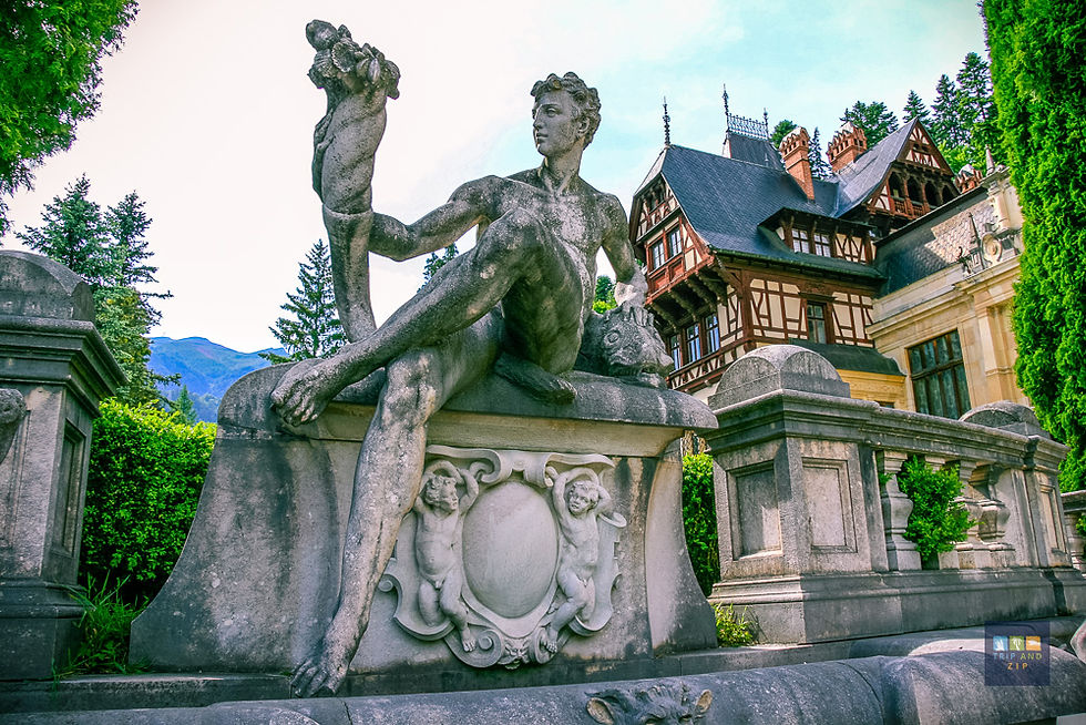 Stone statue of a person holding an object, set against a Tudor-style mansion with trees and mountains in the background.