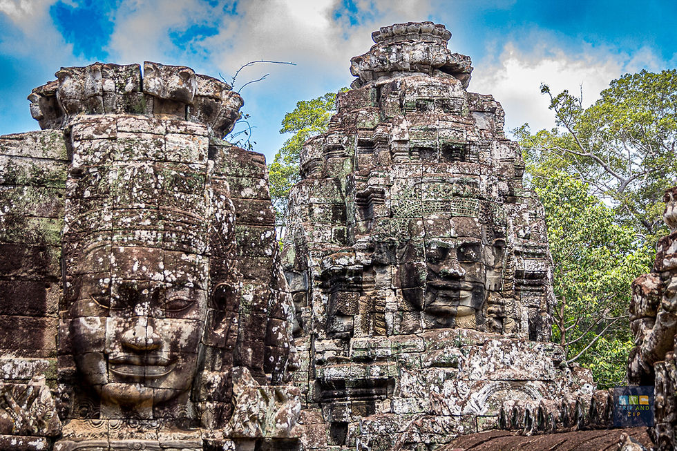 Ancient stone temple with carved faces, set against a blue sky and green trees. The weathered stones create a serene, historical atmosphere.
