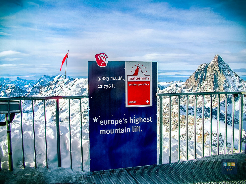 Sign reading "Europe's highest mountain lift" at Matterhorn Glacier Paradise, snowy peaks in background, blue sky, red flag waving.