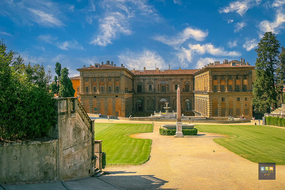 Historic palace with a manicured lawn, central fountain, and an obelisk. Sunny day with blue skies and a few scattered clouds.