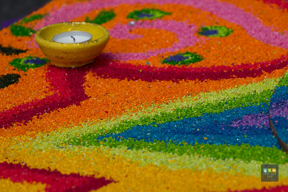 Colorful rangoli pattern with swirling orange, pink, green, and blue hues, featuring a small yellow candle holder on top. Mood is festive.