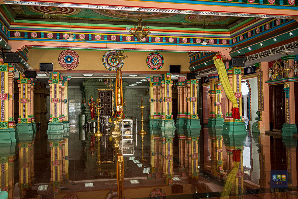 Colorful temple interior with ornate pillars and ceiling designs, reflective glossy floor, golden ceremonial poles, and vibrant decorations.