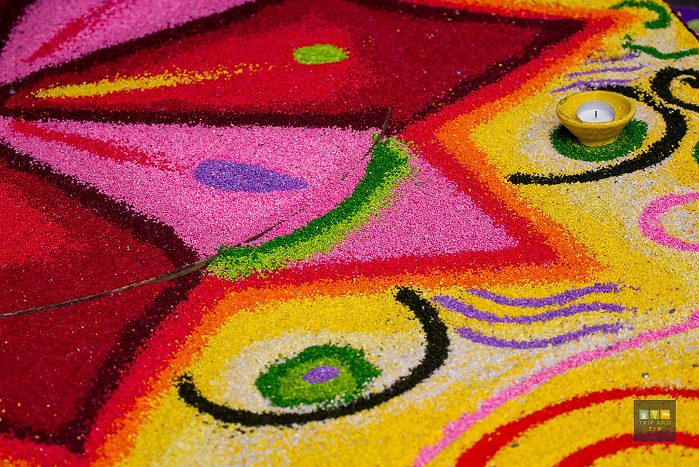 Colorful rangoli pattern with pink, red, yellow hues, concentric shapes, and a single lit candle in a dim setting, evokes festive mood.