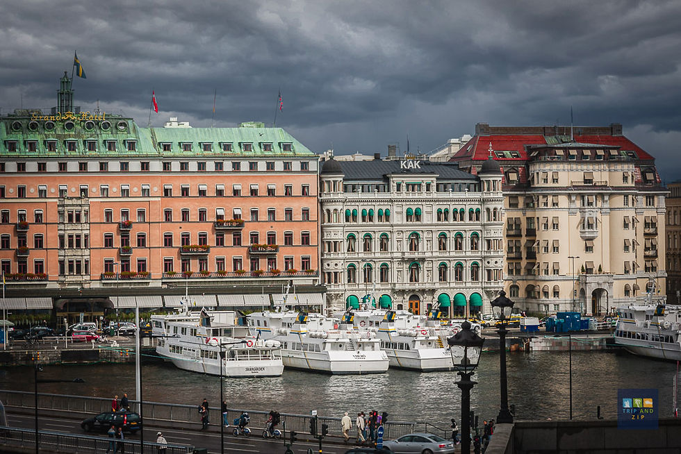 Historic buildings with colorful facades line a waterfront with moored boats. Cloudy skies and pedestrians create a vibrant yet moody scene.