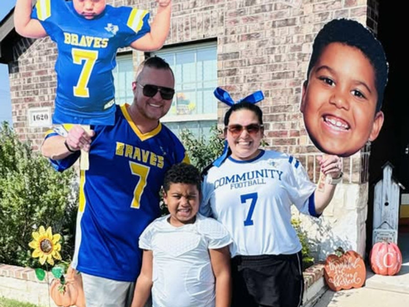 A family in matching jerseys holding a big head cutout of a player
