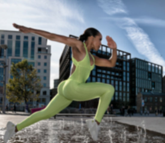 black woman wearing a acid green leotard jumping over a fountain