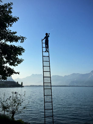 A person standing on the third-last step of a ladder, held by no one and standing at the edge of water, reaches for a shooting star in the distance. In the context of this post, it represents our expectations and how they impact our experience. Image by Armand Khoury.