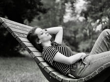 A black and white picture of a young woman wearing a striped t-shirt and a pair of jeans relaxing on an outdoor slatted wooden recliner. This photo by Ashkan Sadeghi is symbolic, in the context of this blog post, of the underrated luxury of boredom.