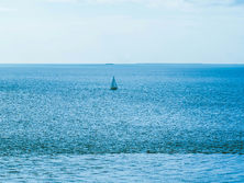 A sailboat seen in the distance on the vast and seemingly endless waters. In the context of this post, this image signifies vastness of the Universe and Time and the smallness of our efforts and lifespans. Image by Mari Duarte.