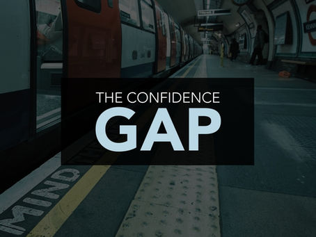 A platform-level photo of a tube station. A train is in the station. Prominent in the foreground is the sign on the platform edge that reads "Mind the gap". Over the image is a panel of bold text that reads "The Confidence Gap".